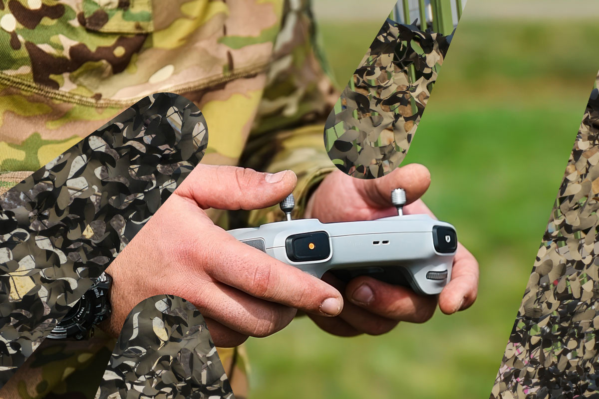 Nærbilde av en soldats hender som holder en fjernkontroll for en drone. Soldaten har kamuflasjeuniform, og bakgrunnen er grønn og uskarp.